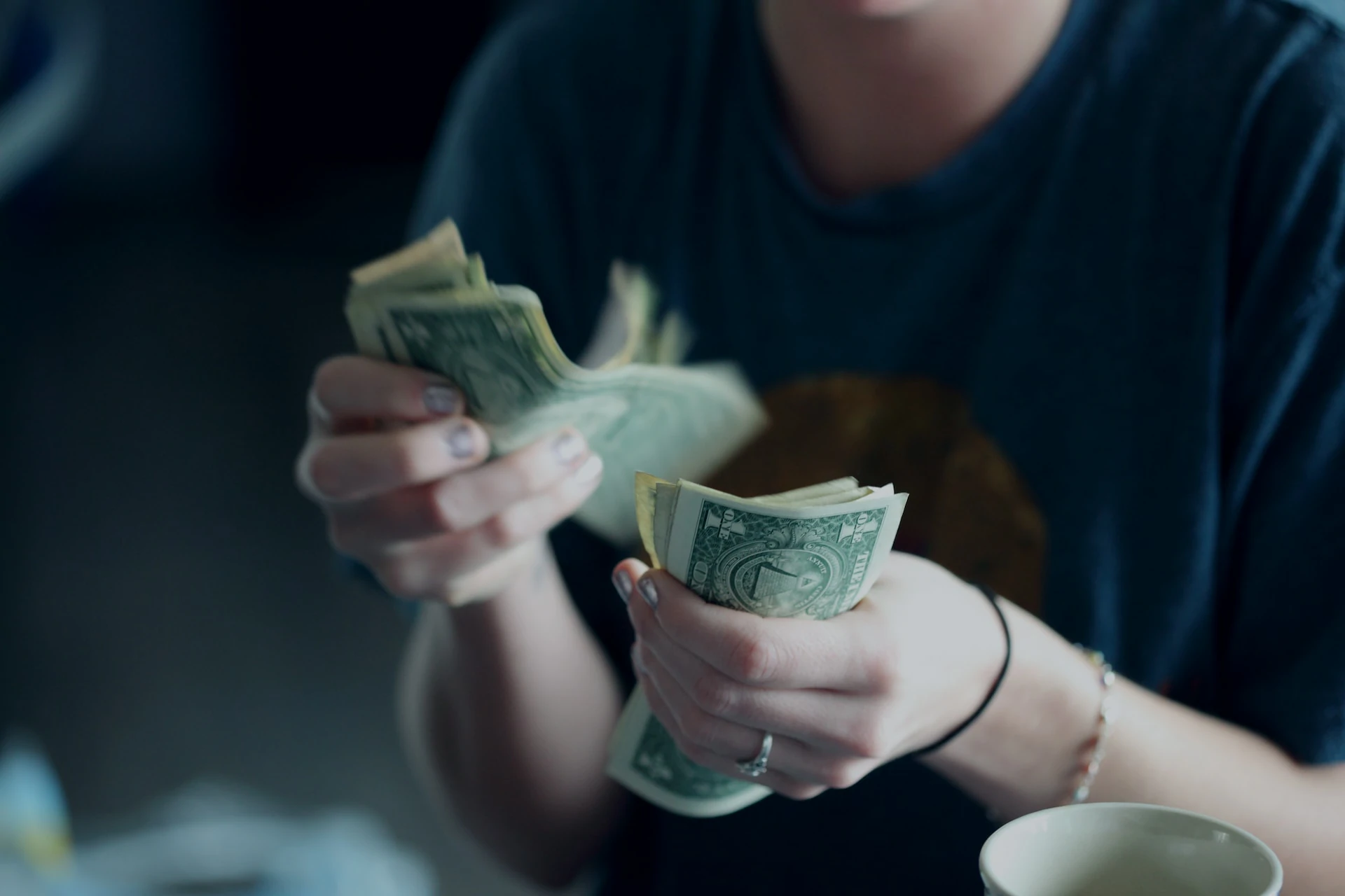 Mãos contando notas de dólar, simbolizando a gestão financeira pessoal. Foto de Alexander Grey na Unsplash